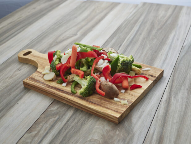 Chopped and sliced mixed vegetables on a wood paddle, close-up