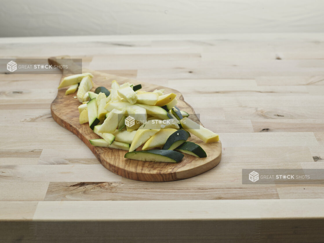 Sliced zucchini and summer squash on a natural wood paddle, close-up