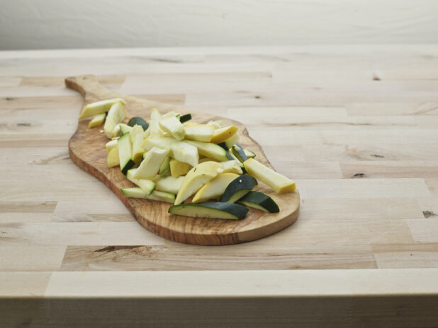 Sliced zucchini and summer squash on a natural wood paddle, close-up