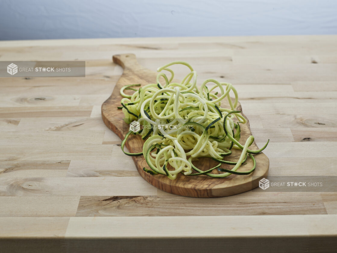 Spiralized raw zucchini noodles in a heap on a wooden paddle, close-up