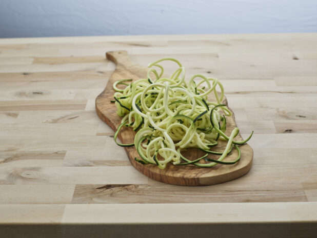 Spiralized raw zucchini noodles in a heap on a wooden paddle, close-up