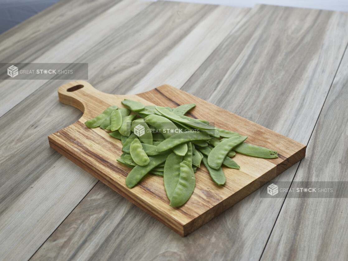 Fresh snow pea pods on a rectangular wood paddle, close-up