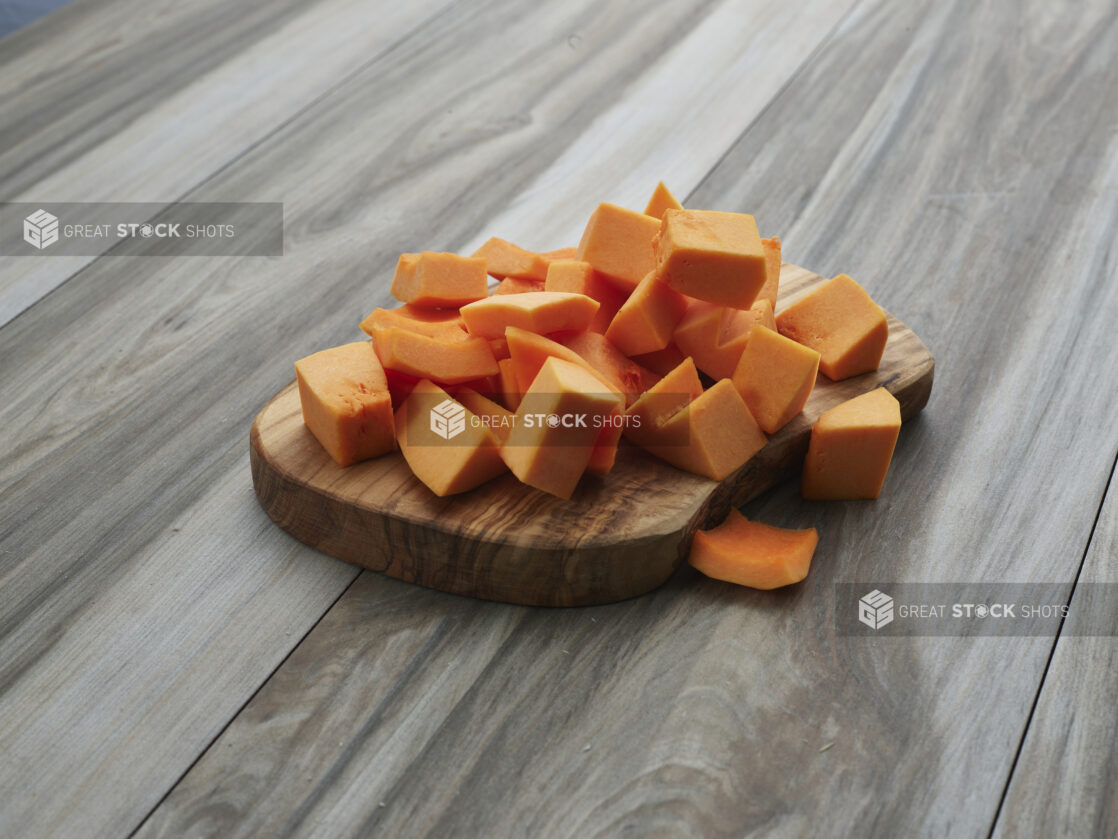 Chopped butternut squash piled on a natural wooden board, close-up