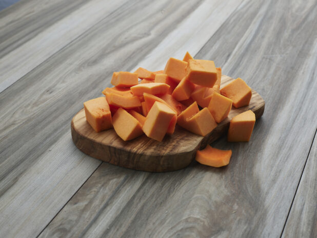 Chopped butternut squash piled on a natural wooden board, close-up
