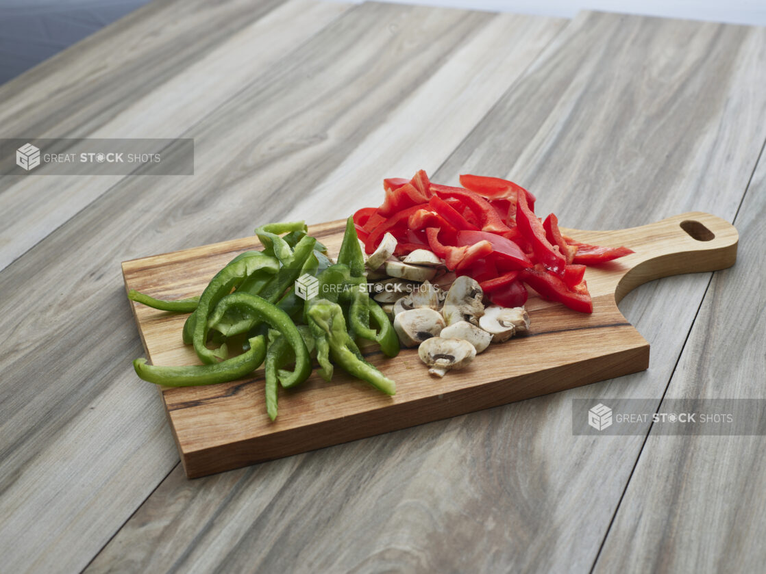 Sliced bell peppers and mushrooms on a wooden paddle, close-up