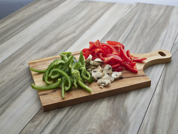 Sliced bell peppers and mushrooms on a wooden paddle, close-up