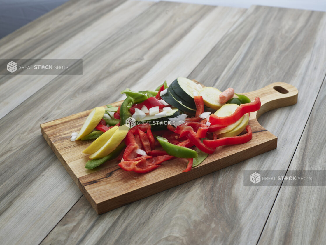 Sliced bell peppers, zucchini, and summer squash piled on a wood paddle, close-up