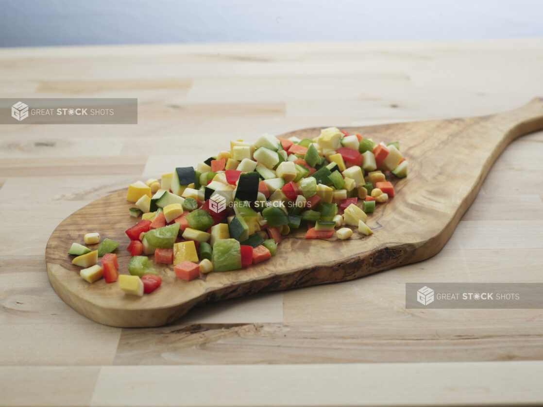 Diced zucchini, summer squash, and bell peppers piled on a wooden paddle, close-up