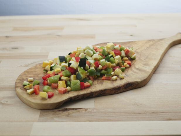 Diced zucchini, summer squash, and bell peppers piled on a wooden paddle, close-up