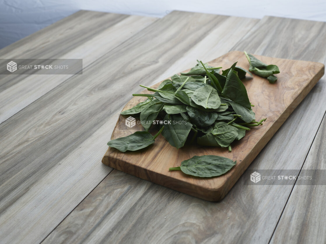 Fresh basil leaves in a pile on a wooden cutting board, close-up