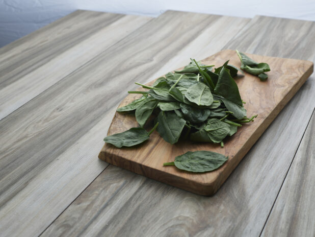 Fresh basil leaves in a pile on a wooden cutting board, close-up