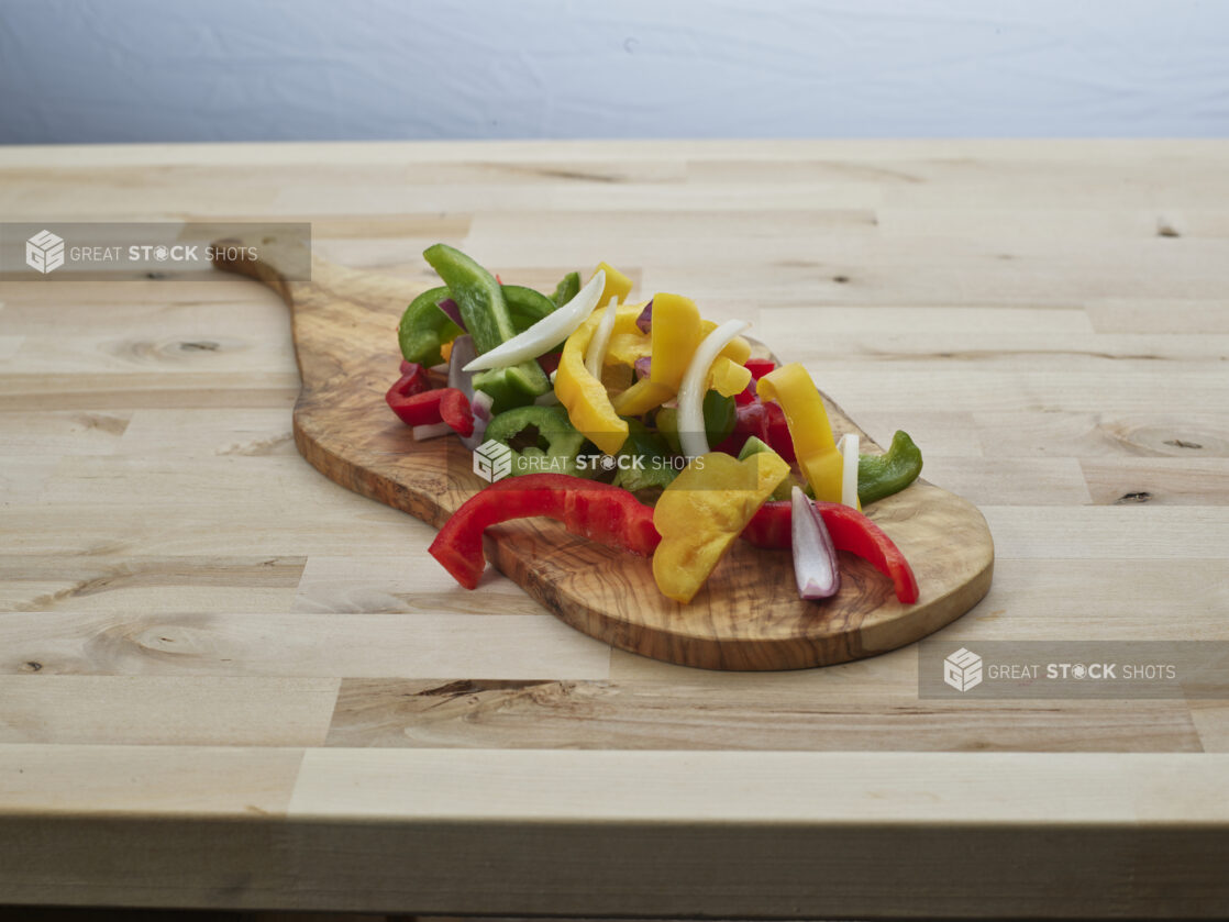 Sliced bell peppers and red onions on a natural wood paddle, close-up