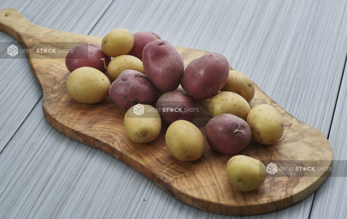 Red and white potatoes piled on a wooden paddle, close-up