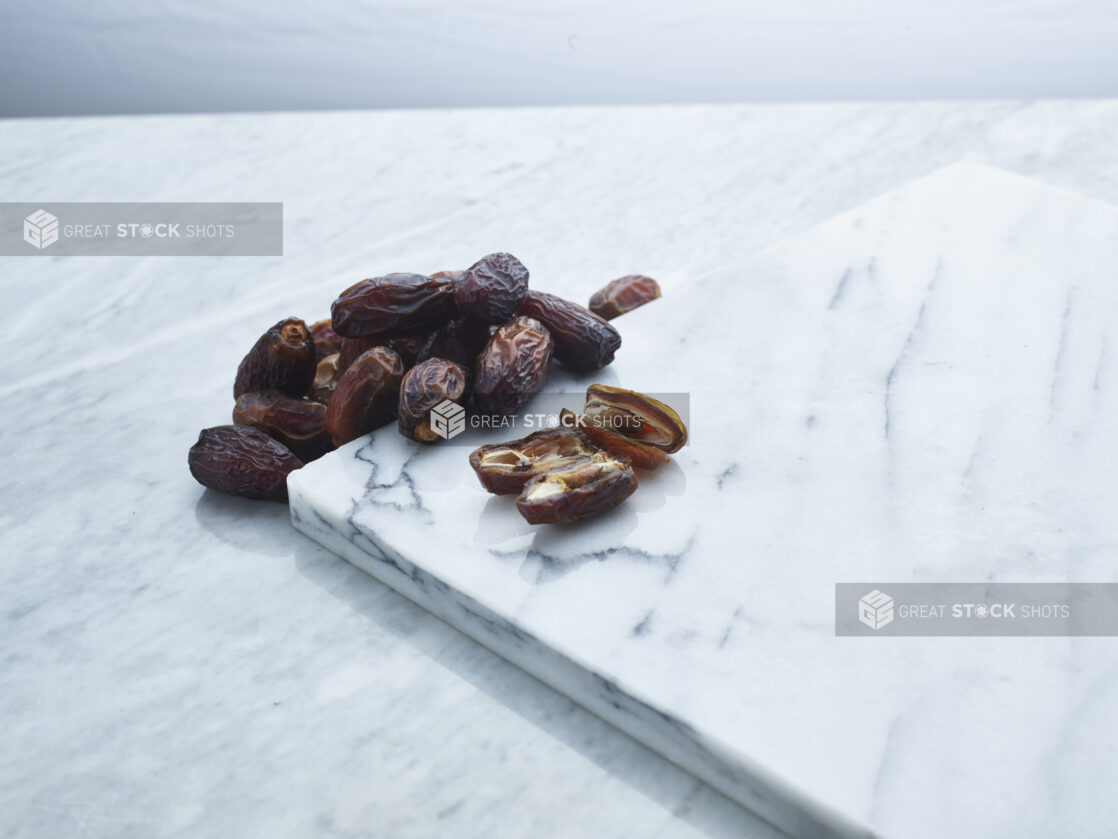 Dates, sliced and whole, on a white marble background