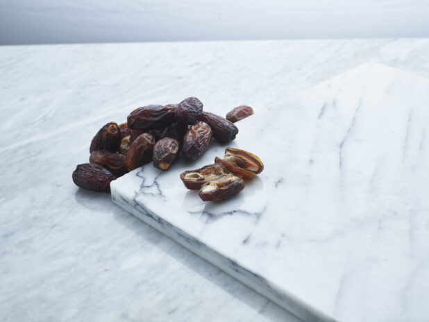 Dates, sliced and whole, on a white marble background