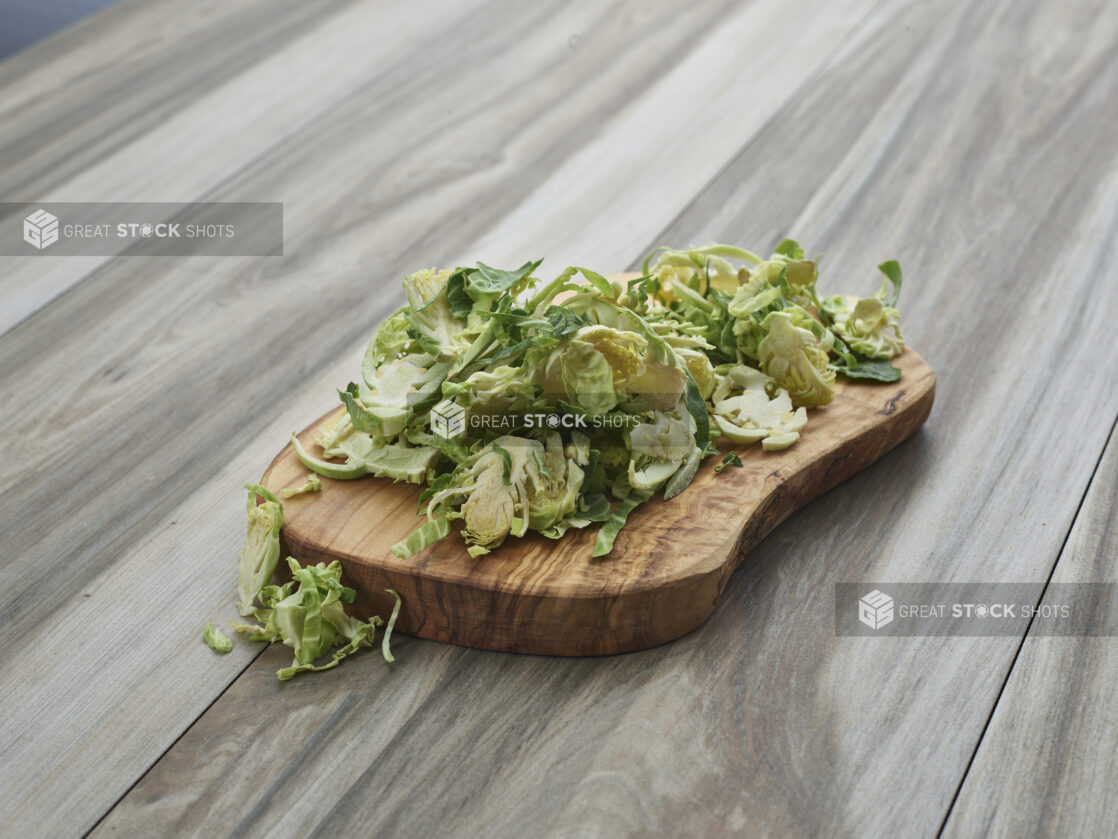 Sliced fresh brussels sprouts piled on a natural wood board, close-up