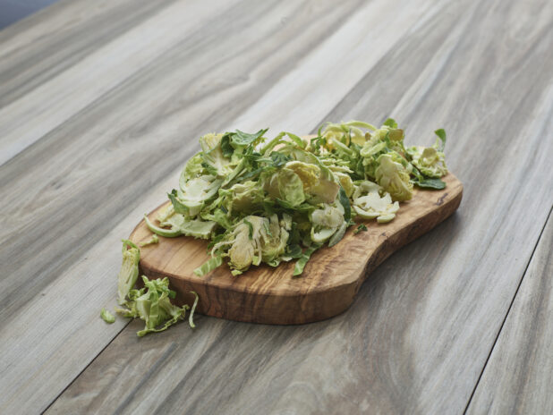 Sliced fresh brussels sprouts piled on a natural wood board, close-up