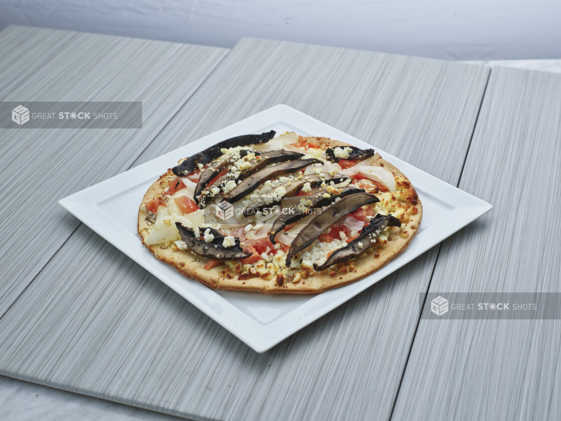 Personal-size thin-crust portobello and cauliflower pizza on a square white plate