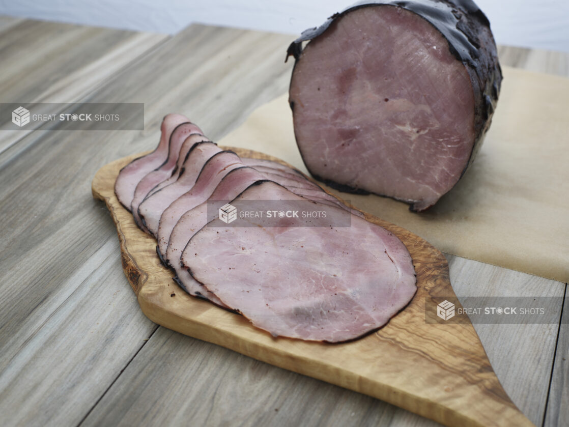 Baked Virginia ham with thin slices arranged on a wooden paddle, close-up