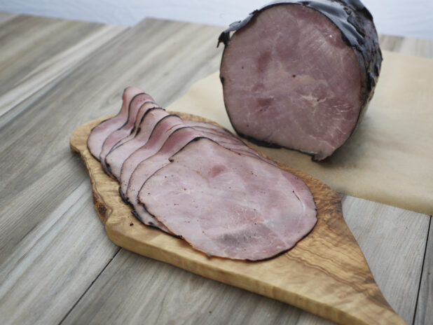 Baked Virginia ham with thin slices arranged on a wooden paddle, close-up