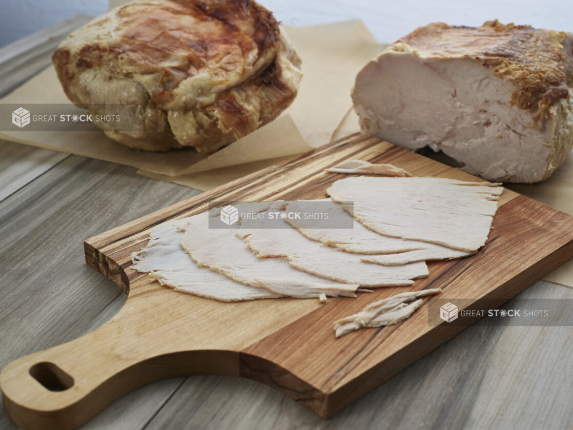 Slices of roast pork arranged on a wooden paddle, close-up, whole and partial roasts in background