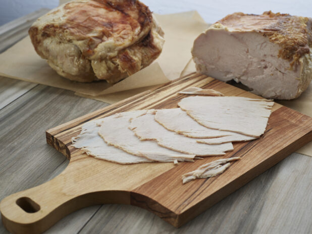 Slices of roast pork arranged on a wooden paddle, close-up, whole and partial roasts in background