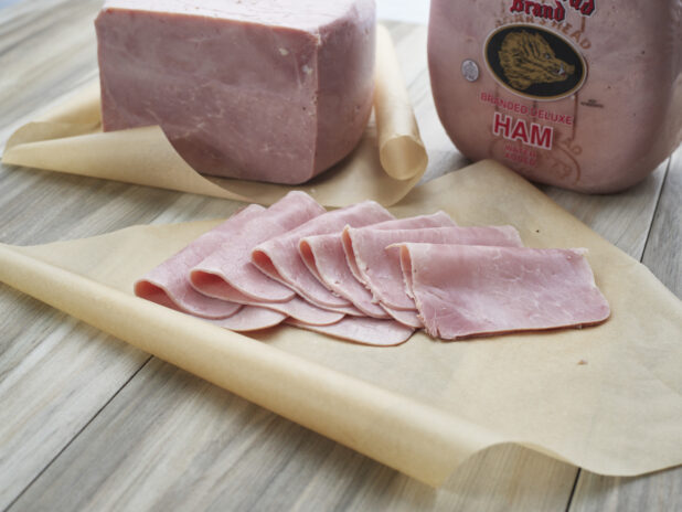 Sliced cooked ham arranged on parchment paper, close-up, whole ham in background