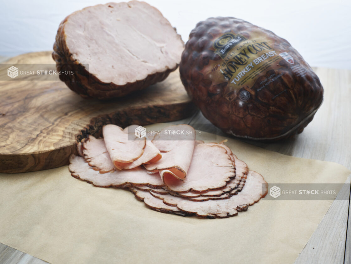 Sliced roast turkey breast arranged on parchment paper, close-up, with whole and half roasts in background