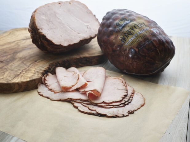 Sliced roast turkey breast arranged on parchment paper, close-up, with whole and half roasts in background