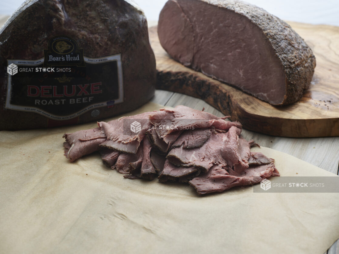 Thinly sliced roast beef on parchment paper, whole roast in background