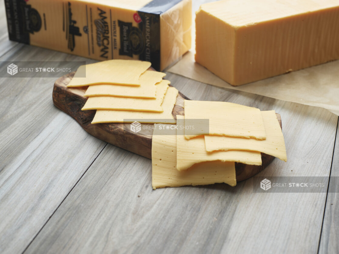 Sliced American cheese arranged on a natural wood board, whole block of cheese in background