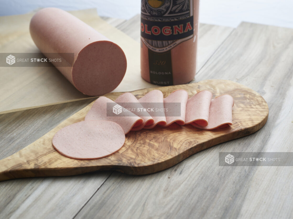 Bologna slices arranged on a wooden paddle, close-up, bologna sausage in background