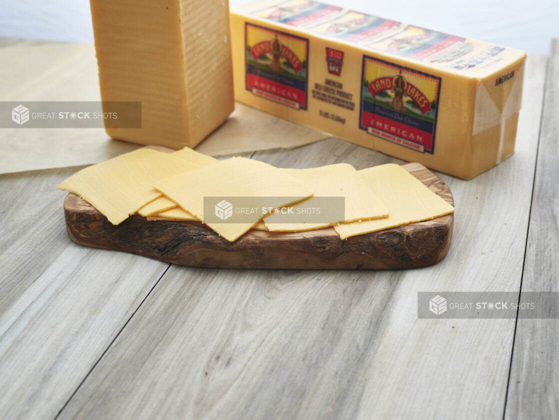 Sliced American cheese arranged on a wood board, close-up, brick of cheese in background