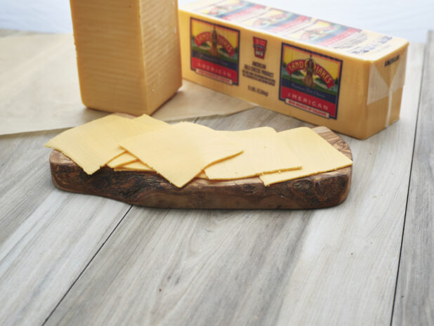 Sliced American cheese arranged on a wood board, close-up, brick of cheese in background