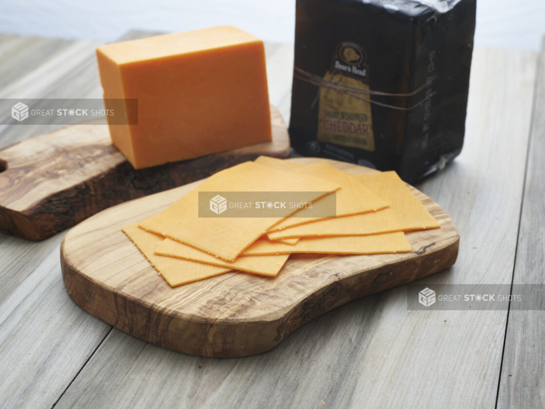 Slices of black wax cheddar cheese arranged on a wooden board, close-up, brick of cheese in background