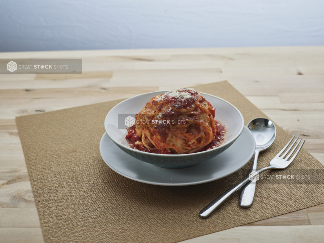 Baked cheesy spaghetti muffin in a small bowl on side plate, close-up