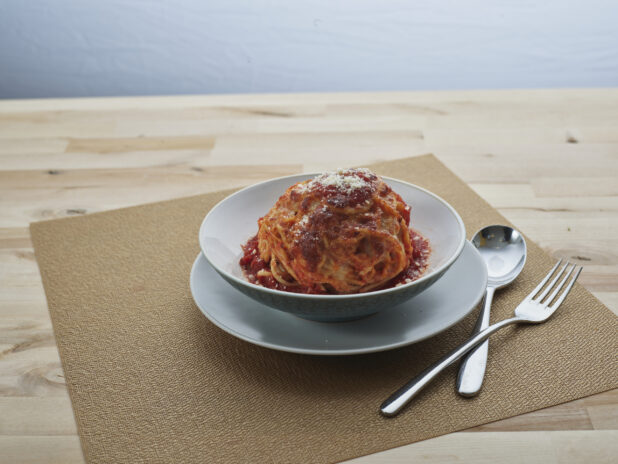 Baked cheesy spaghetti muffin in a small bowl on side plate, close-up