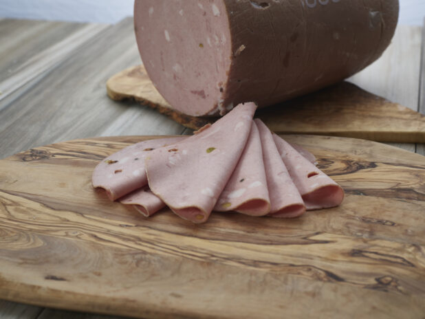 Thin slices of mortadella with pistachios arranged on a wood board, close-up, large piece in background