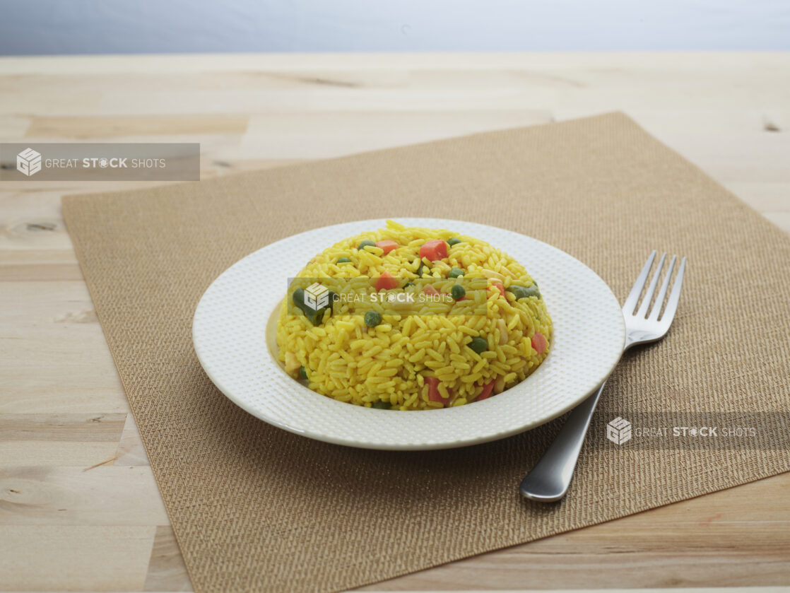 Yellow rice with vegetables in a bowl-shaped mound on a decorative white plate