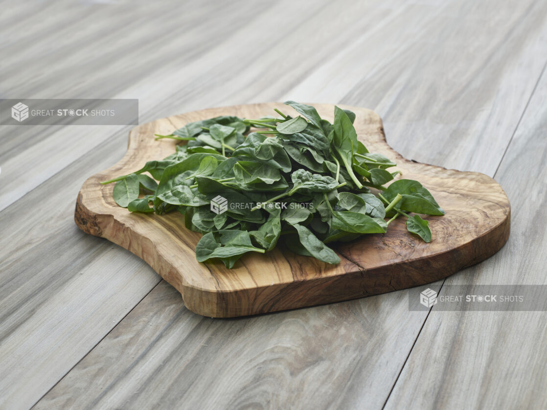 Fresh baby spinach piled on a natural wooden board, grey wood background