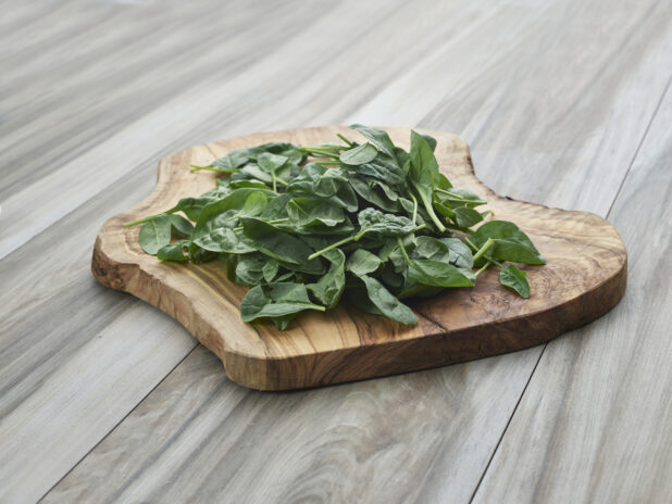 Fresh baby spinach piled on a natural wooden board, grey wood background