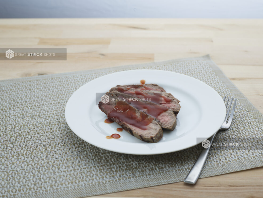 Slices of London broil steak with barbecue sauce arranged on a white plate