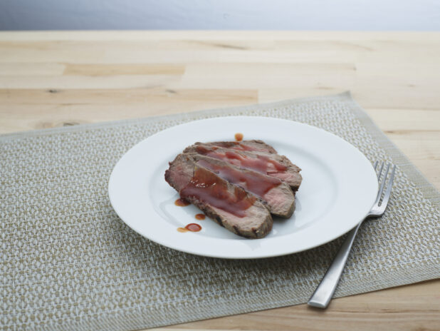 Slices of London broil steak with barbecue sauce arranged on a white plate