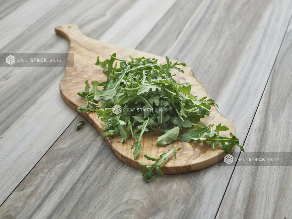 Fresh arugula piled on a wood paddle