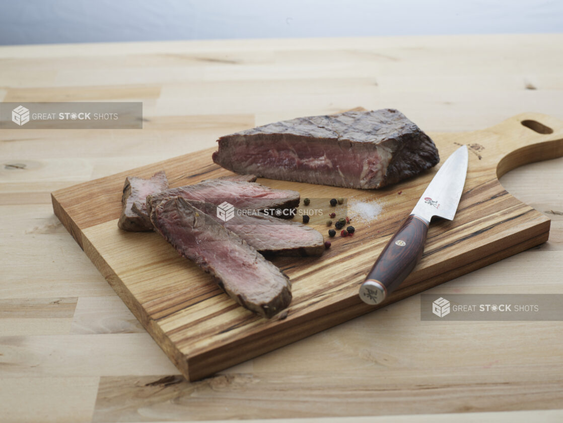 London broil steak partially sliced with seasonings and a Japanese knife on a wooden paddle