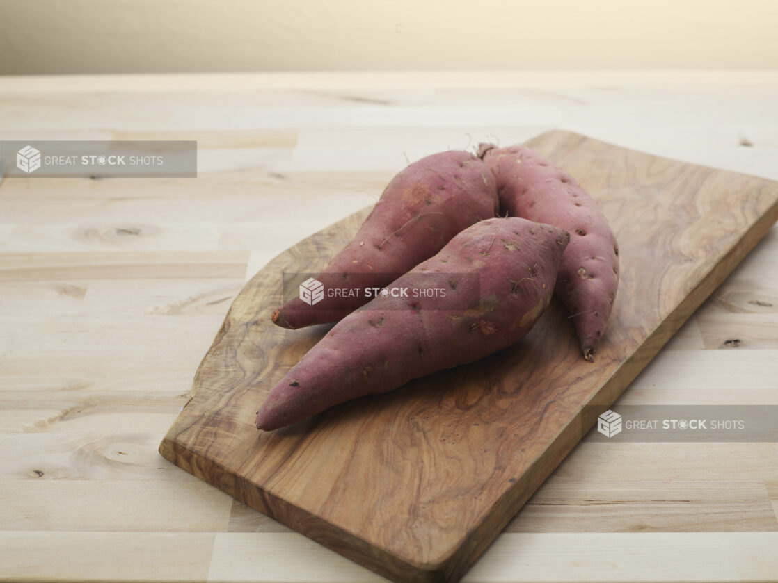 Three sweet potatoes on a wood cutting board, wood background