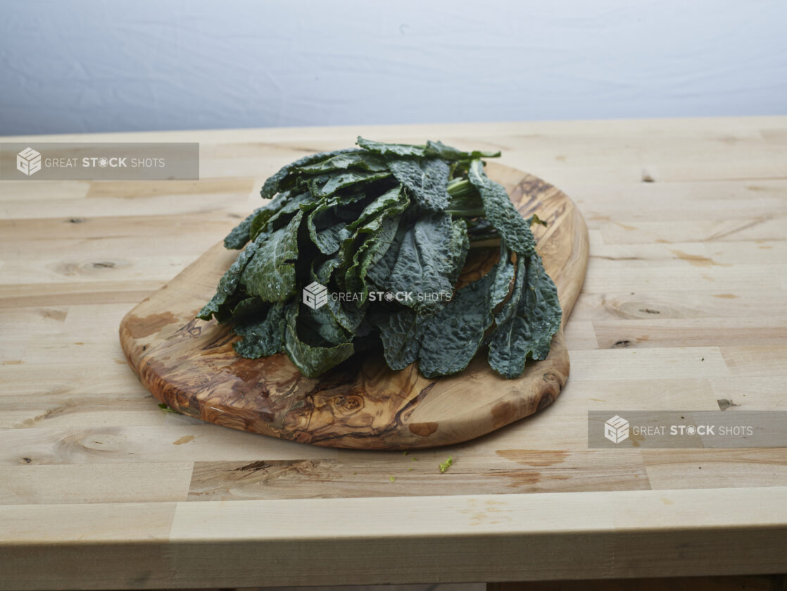 Fresh lacinato kale piled on a natural wood board, wood background