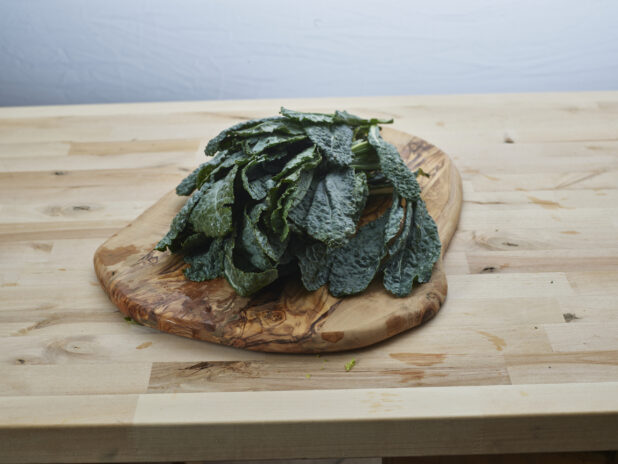 Fresh lacinato kale piled on a natural wood board, wood background