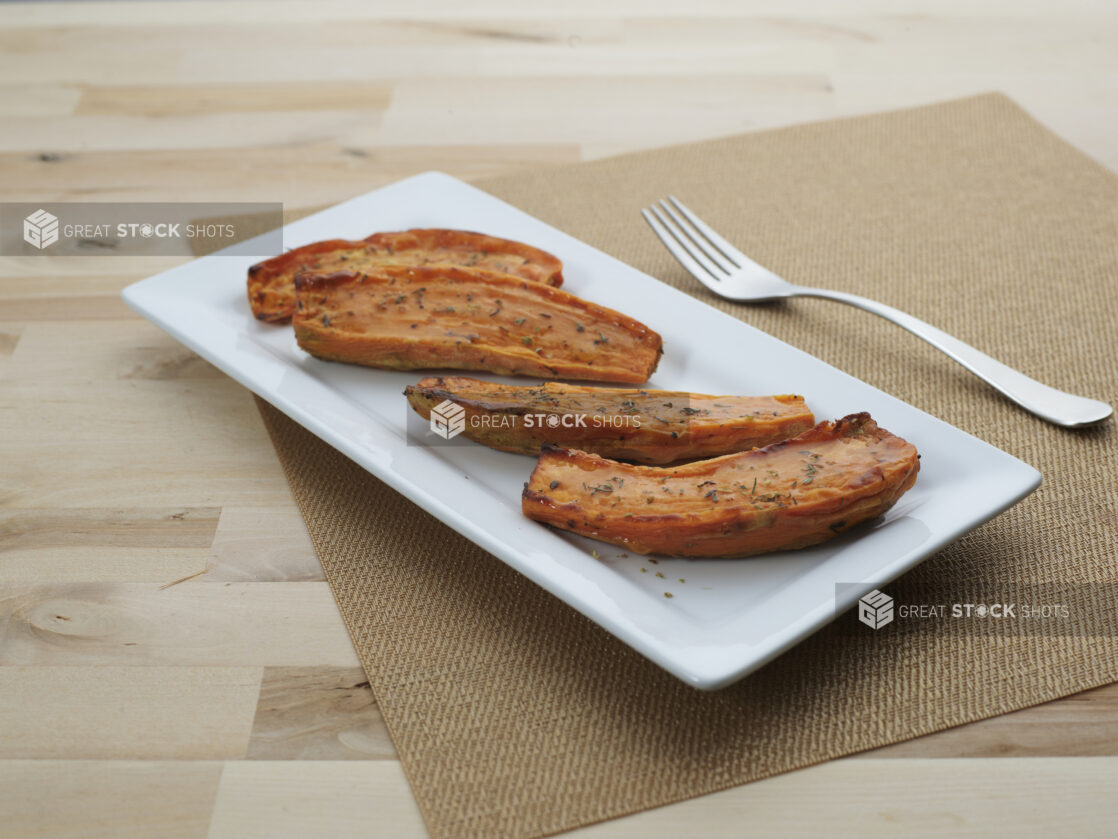 Baked sweet potatoes, halved, on a rectangular white platter, close-up