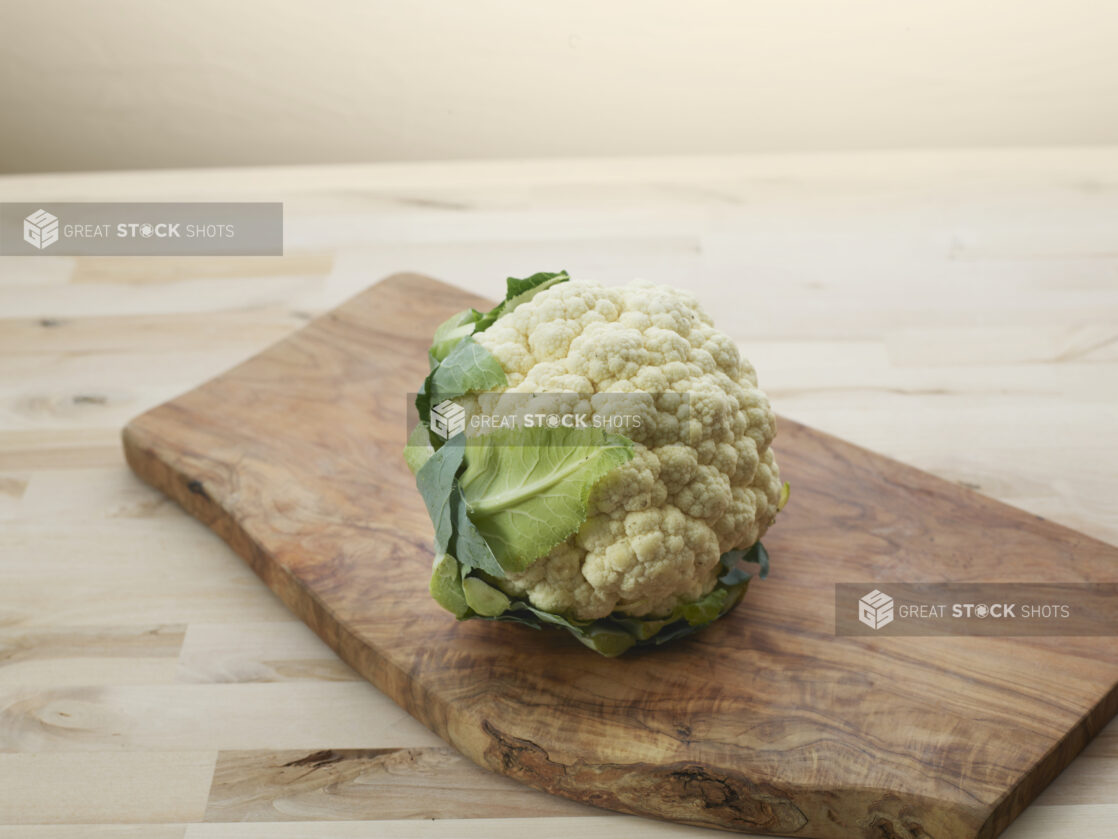 Whole fresh cauliflower on a curved wooden board, close-up